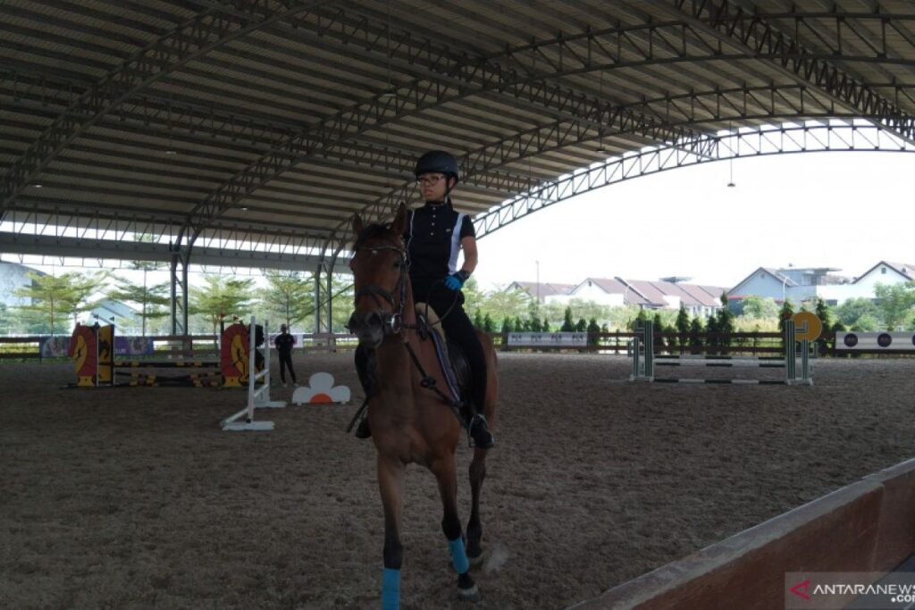 Anak sedang menunggang kuda di arena indoor di Sekolah Berkuda Equinara dengan perlengkapan berkuda lengkap.